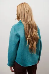 Chaqueta de paño color gris oscuro, con solapas amplias y cierre frontal mediante un alamar único. Presenta bolsillos laterales y mangas largas con puños rectos.