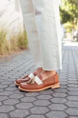 Mocasines de cuero color tostado, con detalle de antifaz en cuero crudo y borlas decorativas. Hechos a mano en Uruguay.