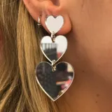 Aros colgantes plateados con tres dijes en forma de corazón de distintos tamaños.
