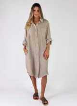 Camisola midi confeccionada en lino color tostado, con cierre frontal de botones, bolsillos laterales y un bolsillo aplicado en el pecho. Presenta mangas largas con trabilla para sujetar remangadas y cuello camisero.