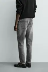 Pantalón de jean corte slim fit, color gris con efecto lavado. Presenta diseño de cinco bolsillos, cierre frontal con cremallera y botón, y tejido elástico.