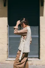 Chaleco tejido de lana rústica en color crudo, con cuello en V y aberturas laterales ajustables con lazos.