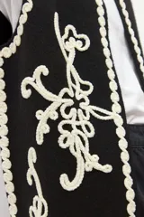 Chaleco tejido negro con escote en V, sin mangas y bordados en color crema con motivos florales y detalles de ondas en los bordes.