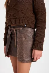 Minifalda de cuero con efecto desgastado, de silueta recta y diseño de capas frontales superpuestas. Incluye un lazo ajustable en la cintura que pasa por ojalillos metálicos y bolsillos laterales integrados.