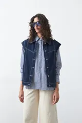 Chaleco de jean en tono celeste claro, con corte recto, cuello camisero, cierre frontal con botones metálicos y costuras visibles.