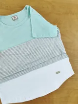 Remera de manga corta con diseño de bloques de color: celeste en la parte superior, gris a rayas horizontales en el medio y blanco en la parte inferior.