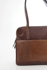 Cartera de hombro tipo portafolio confeccionada en cuero vacuno, con diseño estructurado que combina marrón liso y un panel frontal en cuero texturizado color mostaza. Posee doble asa larga y cierre superior.