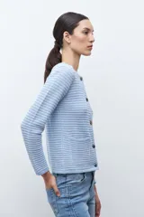 Chaqueta de punto color celeste, con cuello redondo, manga larga y cierre frontal con botones metálicos plateados.