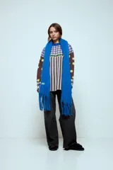 Bufanda de textura suave y acabado afelpado, con diseño liso y flecos en los extremos. Incluye una pequeña etiqueta decorativa en uno de los laterales.