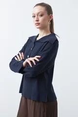 Sweater de tejido de punto color azul marino, con cuello polo amplio y cierre frontal con tres botones metálicos. Presenta mangas largas levemente acampanadas y un diseño de silueta relajada con aberturas laterales en el ruedo.