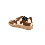 Sneaker de diseño artesanal confeccionada en cuero con pelo natural con estampado de manchas tipo vaca en tonos marrón y blanco. Presenta cordones al tono y suela de goma color caramelo.