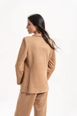 Blazer de gamuza con solapas clásicas, cierre frontal de doble botón y bolsillos laterales. Presenta un corte estructurado con hombreras.