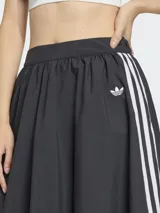 Falda larga de estilo deportivo con silueta voluminosa tipo globo, confeccionada en tejido técnico color negro. Presenta el diseño clásico de tres rayas blancas laterales y el logo del trébol bordado. Cuenta con cintura elástica y cierre lateral.
