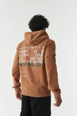 Campera con capucha de felpa color marrón, con estampado tipográfico en la espalda, bolsillo tipo cargo en la manga y puños elásticos.