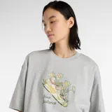 Remera gris de algodón con cuello redondo y mangas cortas. Estampado frontal con un champión New Balance rodeado de flores y el logo de la marca.
