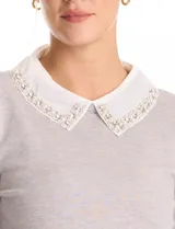 Buzo de punto fino color gris, con cuello camisero de gasa integrado decorado con apliques de perlas y brillos. Presenta mangas largas y puños acanalados.