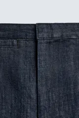 Pantalón de corte barrel fit confeccionado en denim de algodón rígido color azul oscuro. Presenta cintura con pliegues frontales, bolsillos laterales y bolsillos traseros de vivo. Cierre frontal con cremallera y gancho metálico oculto.