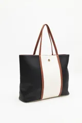 Cartera tipo tote bag en símil cuero, con diseño en bloques de color negro y blanco, y detalles en marrón. Tiene asas largas para llevar al hombro y un cierre magnético.