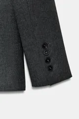 Blazer entallada de color gris oscuro, confeccionada en tejido con algodón. Presenta un cuello solapa con aplicación de pelo sintético desmontable, manga larga, bolsillos delanteros con solapa y cierre frontal con botones.