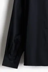 Camisa negra de satén con cuello inglés, tapeta lisa, bolsillo superior abierto y canesú en la espalda. Mangas largas con puños abotonados y bajo recto. Corte estándar.
