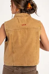 Chaleco de denim color camel con efecto lavado, cuello camisero, cierre frontal con botones metálicos y dos bolsillos frontales con solapa.