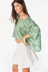 Blusa de lino italiano color blanco, con diseño holgado, escote asimétrico estilo off-shoulder y mangas cortas amplias.