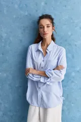 Camisa celeste de calce relajado, con cuello camisero, bolsillo aplicado en el pecho y mangas largas con puños abotonados. Cuenta con lazos ajustables en los laterales para fruncir y regular la silueta.