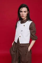 Chaleco blanco de denim con diseño cruzado asimétrico y cierre frontal con tres botones carey.