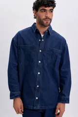 Sobrecamisa de jean color azul oscuro, de corte oversize, con mangas largas, bolsillos frontales con solapa y cierre con broches a presión.