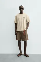 Camiseta relaxed fit color beige, con cuello redondo y manga corta. Presenta un bordado y estampado combinado a contraste en el delantero y la espalda.