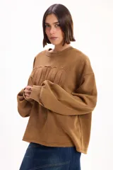 Buzo oversize color marrón con cuello redondo, mangas largas amplias y puños acanalados. Presenta letras en relieve con efecto desflecado en el frente y ruedo con terminación desflecada.