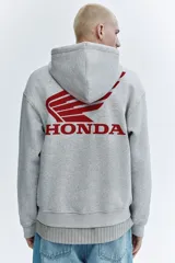 Campera con capucha gris melange de felpa con interior cepillado, cierre frontal, hombros caídos y bolsillos tipo canguro. Presenta estampado pequeño de Honda en el pecho.