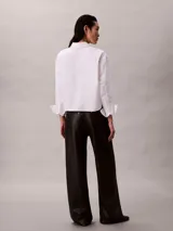 Pantalón negro de pierna ancha con efecto piel, talle medio y diseño clásico de cinco bolsillos, cierre de botón y cremallera.