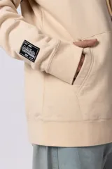Buzo canguro color bordó con capucha y cordones ajustables. Presenta un bolsillo frontal tipo canguro y un pequeño parche rectangular con diseño gráfico en la manga derecha.