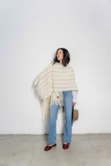 Ruana color crudo con diseño tejido a rayas verticales en tonos beige y flecos en el borde inferior.