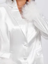 Blazer blanco de satén con solapas clásicas, cierre frontal de botones y puños decorados con plumas blancas. Presenta un corte estructurado y elegante.