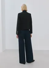 Chaqueta negra de corte estructurado con cuello mao, cierre frontal con botones dorados y mangas largas con botones decorativos en los puños.