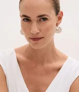 Par de caravanas con diseño circular abierto, confeccionados en metal con baño dorado. Presentan una pieza de nácar en forma de semicírculo y un detalle de strass en el centro.