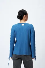 Sweater color crema de tejido de canalé con detalle de trenzado en las mangas y terminación con lazo ajustable.