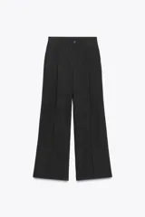 Pantalón de tiro alto color rojo vibrante, de corte ancho y pierna recta, con pliegues marcados en la parte delantera. Presenta cierre frontal con botón y cremallera, y bolsillos delanteros.