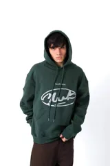 Hoodie de color verde oscuro confeccionado en friza, con capucha, cordones ajustables y bolsillo canguro. Presenta una estampa frontal blanca con el texto 'AnmeEdition' y 'CLUB' en un diseño ovalado de estilo desgastado.