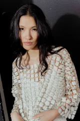 Blusa de red en color blanco con apliques de flores tridimensionales en toda la prenda. Presenta transparencias, cuello redondo y mangas largas.