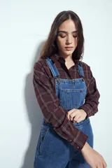 Camisa tipo leñadora de corte oversize, con estampado de cuadros en tonos negro y marrón. Presenta cuello clásico, cierre frontal con botones y mangas largas con puños abotonados.