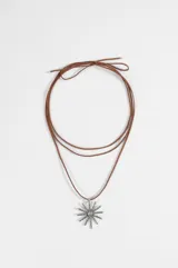 Collar de estilo boho con cordón largo de gamuza color tostado y dije central de metal plateado con forma de sol texturado.