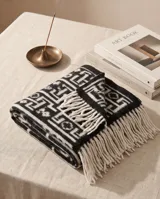 Poncho de lana negro y blanco con diseño geométrico y flecos en el borde inferior.