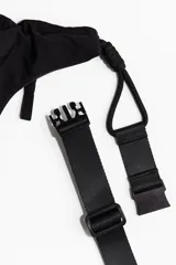 Cartera de nylon color negro, con forma de media luna o banana, diseñada para llevar al hombro. Posee correa ajustable con cierre a presión de plástico y cordones decorativos en color contrastante. Cuenta con un compartimento principal con cierre y un bolsillo interior con cierre.