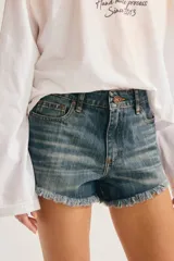 Short de denim azul con efecto desgastado, tiro medio, bolsillos clásicos y terminación de ruedo deshilachado.