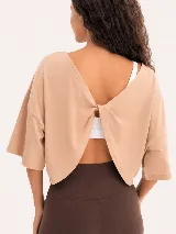 Remera de algodón color beige con diseño de espalda abierta y detalle de nudo torzado. Presenta mangas cortas con corte holgado y estilo casual.