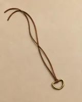 Gargantilla de cuero marrón con dije en forma de argolla metálica dorada.