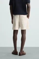 Bermuda de calce regular, color beige claro, confeccionada en tejido de mezcla de algodón con textura jacquard. Presenta cintura elástica ajustable con cordón, bolsillos frontales y un bolsillo trasero de vivo.
